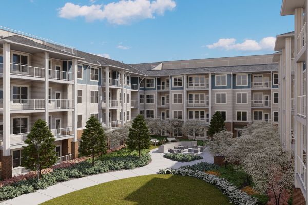 Attain on 5th apartment homes with Modern apartment complex courtyard with green lawn, flowering trees, shrubs, and outdoor seating surrounded by four-story buildings under blue sky.